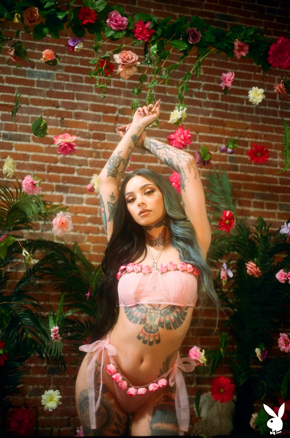Taylor White exposes her inked body in front of a wall of flowers